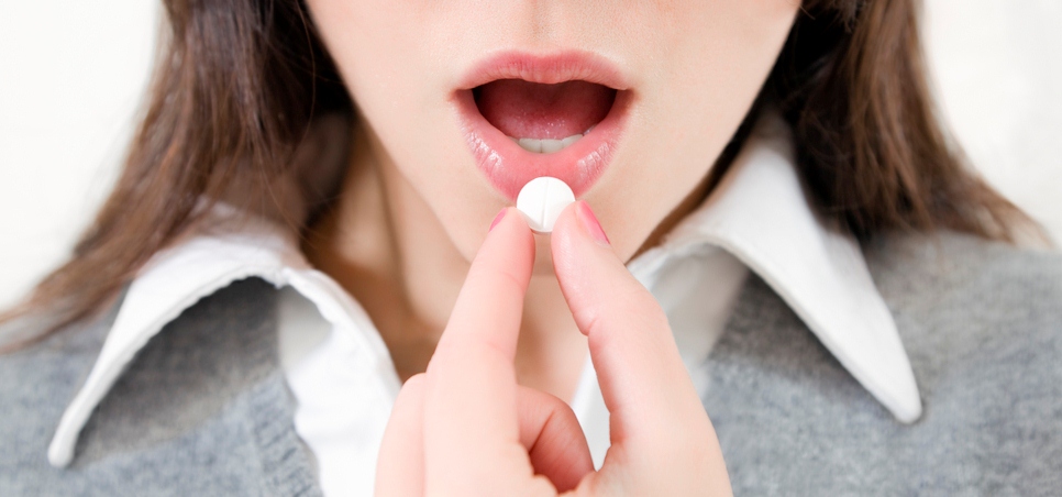 Close-up of young woman putting pill in mouth